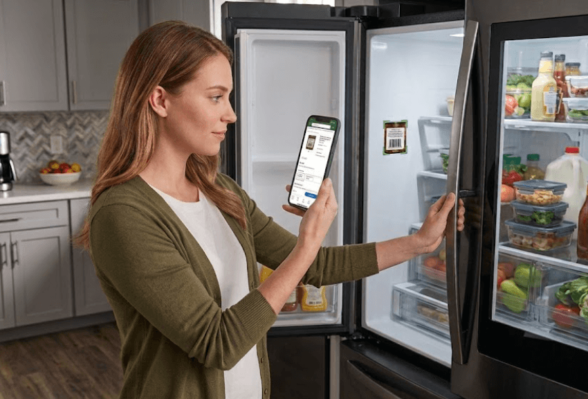 Homeowner checking kitchen inventory on their phone while stocking the fridge